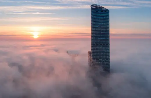 Najwyższy budynek we Wrocławiu wyłania się z porannych mgieł, otoczony różowymi chmurami i wschodzącym słońcem.