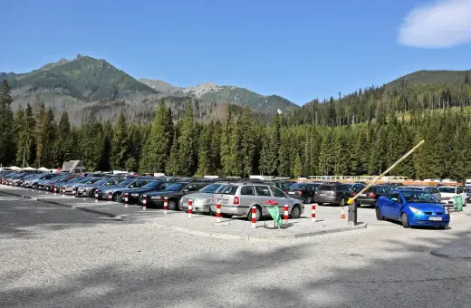 Parking pod Morskim Okiem, pełen samochodów, z górami i lasem w tle.