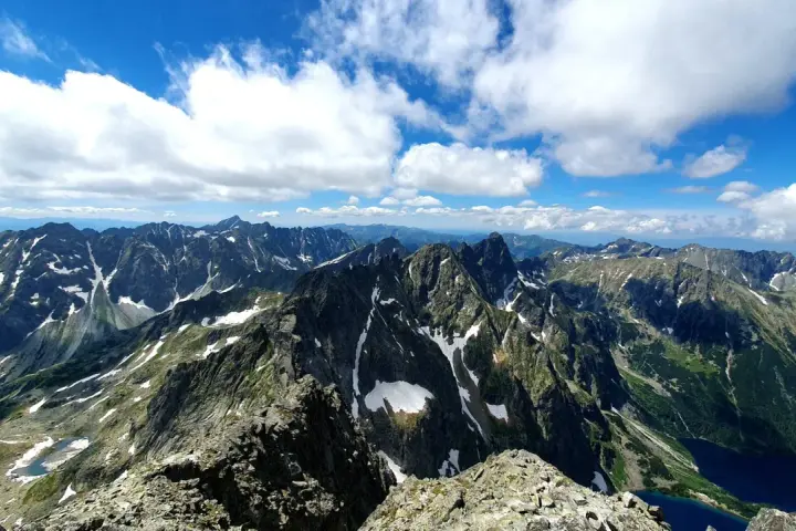 Widok na Tatry Wysokie od strony słowackiej. W oddali widać parking, a bliżej skaliste szczyty z resztkami śniegu.