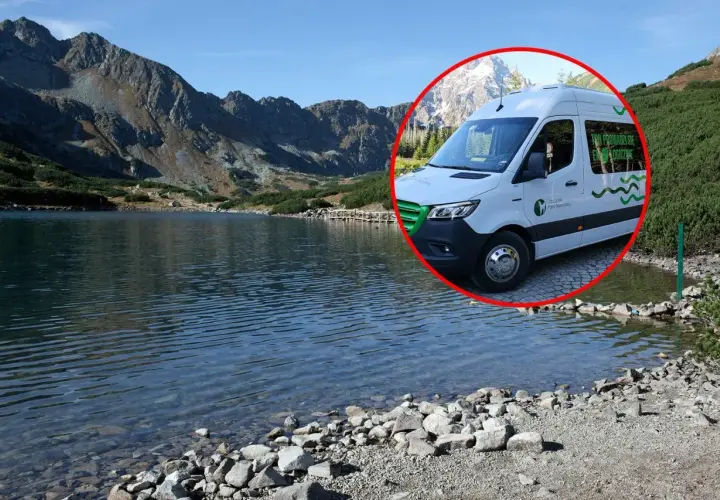 Biały bus do Morskiego Oka stoi przy tafli jeziora, w tle góry.