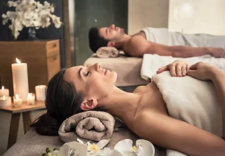 Para relaksu w spa: para leży na stołach do masażu, otoczona świecami i kwiatami. To idealne miejsce, by zapomnieć o codzienności.