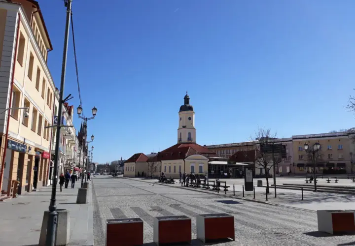 Słoneczny dzień na Rynku Kościuszki w Białymstoku. W oddali wieża ratusza, po bokach kamienice i brukowana nawierzchnia.