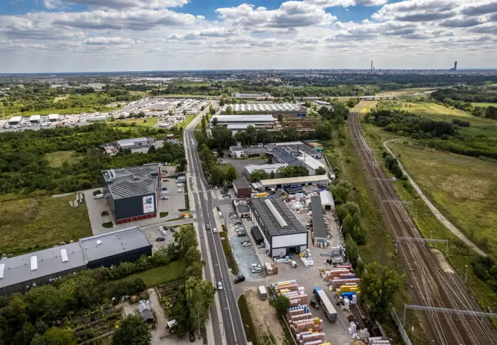 Widok z lotu ptaka na przemysłową okolicę z magazynami, torami kolejowymi i drogą. W oddali widać miasto. To miejsce, gdzie psy mają swoje psie pole.