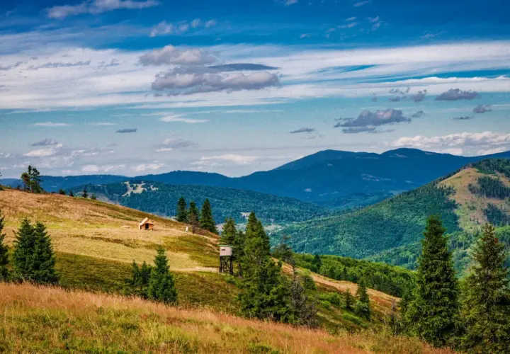 Widok na malowniczą **przełęcz Przegibek** z drewnianą chatką i wieżą widokową na zboczu. W tle gęsto zalesione góry pod błękitnym, chmurnym niebem.
