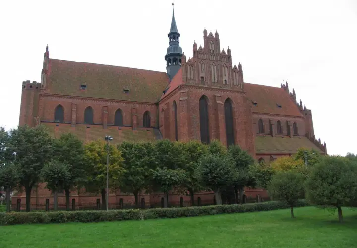 Gotycka katedra w Pelplinie, ceglana budowla z charakterystyczną wieżą i strzelistymi oknami, otoczona zielenią.