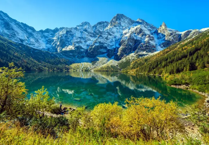 Morskie Oko, Tatry. Turkusowa tafla jeziora odbija ośnieżone szczyty. Widoczna głębokość wody i jesienna roślinność.