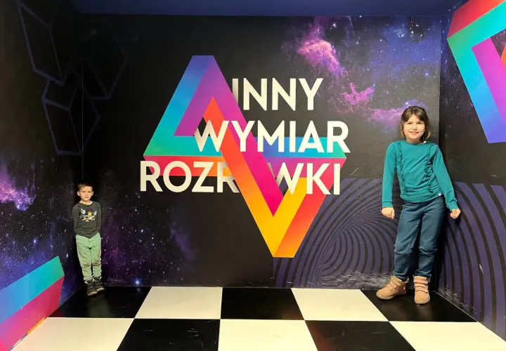 Dzieci w "Innym Wymiarze Rozrywki" w Warszawie. Kolorowa ściana z motywem kosmosu i geometrycznymi kształtami.
