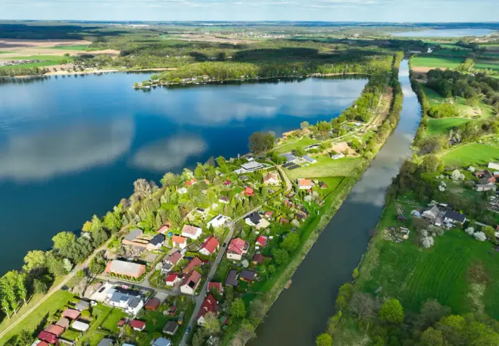 Malownicze pławniowice jezioro otoczone zielenią i domkami letniskowymi, z kanałem wodnym biegnącym równolegle.