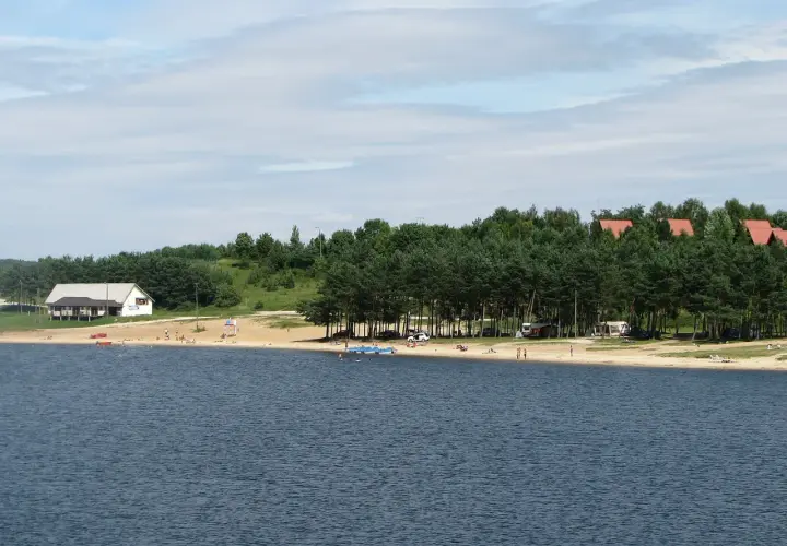Słoneczny dzień nad zalewem Chańcza. Plaża z ludźmi, domki letniskowe i las.