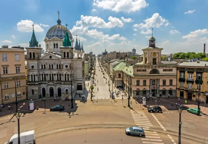 Widok na plac wolności w Łodzi z monumentalną katedrą po lewej i długą ulicą pełną ludzi i samochodów.