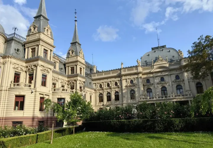 Imponujący pałac poznańskiego, z wieżyczkami i bogatymi zdobieniami, otoczony zielonym ogrodem z kwitnącymi krzewami róż.
