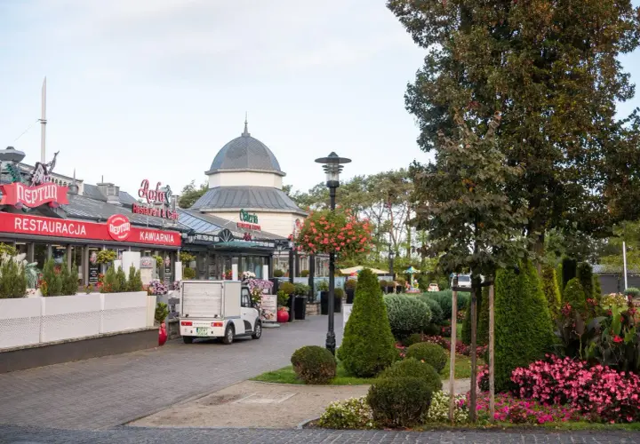 Spacer po alei gwiazd w Międzyzdrojach, z restauracjami i kawiarniami po lewej stronie, a zielenią i drzewami po prawej.