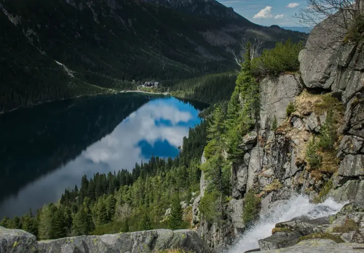 Widok na Morskie Oko z góry, z wodospadem po prawej. Trasa turystyczna prowadzi wzdłuż jeziora otoczonego lasem i górami.