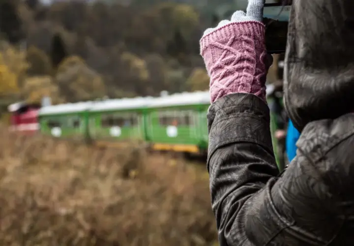 Osoba w różowych rękawiczkach fotografuje zielono-czerwony pociąg. Która kolejka bieszczadzka, która trasa ciekawsza?