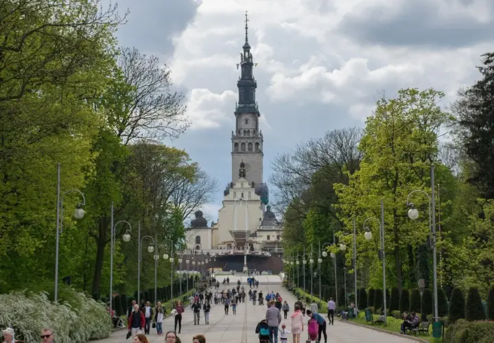 Aleja prowadząca do Jasnej Góry, jednego z najważniejszych sanktuariów maryjnych w Polsce. Ludzie spacerują w kierunku imponującej wieży klasztornej.