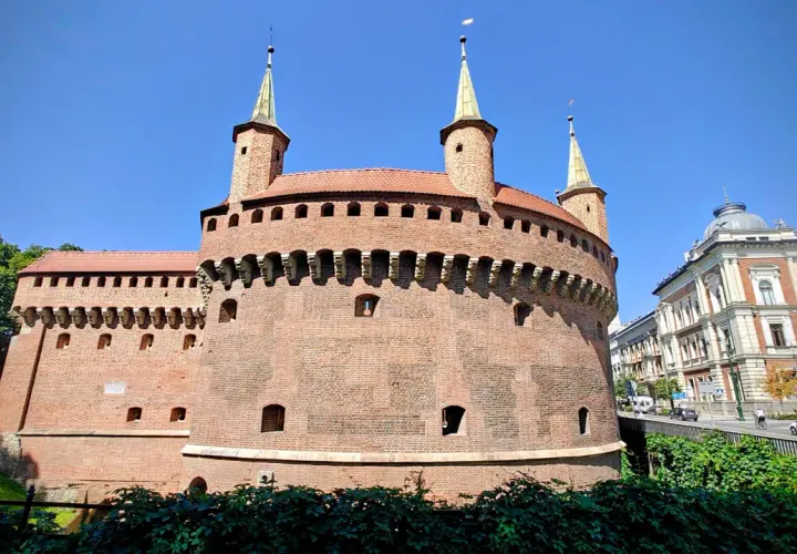 Krakowski zabytek przy Bramie Floriańskiej, okrągła baszta obronna z cegły, góruje nad zielonymi terenami i ulicą.