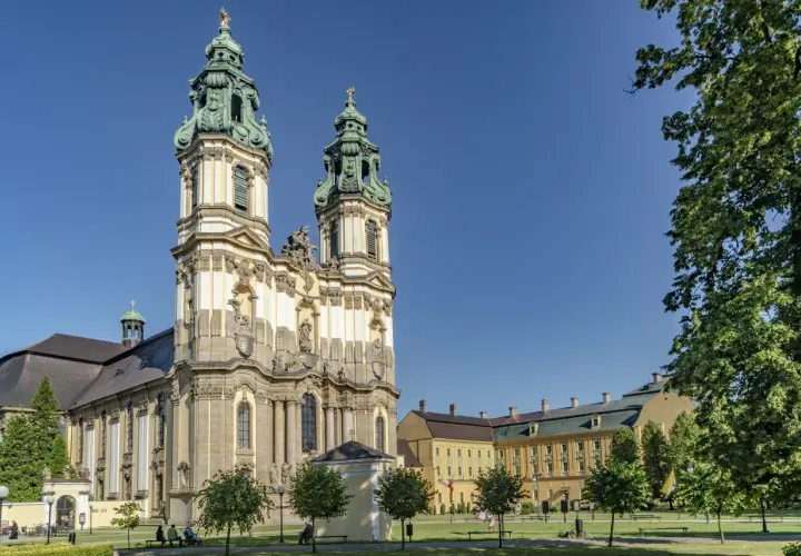 Barokowy zespół klasztorny w Krzeszowie z dwiema wieżami i rozległym skrzydłem, otoczony zielenią.