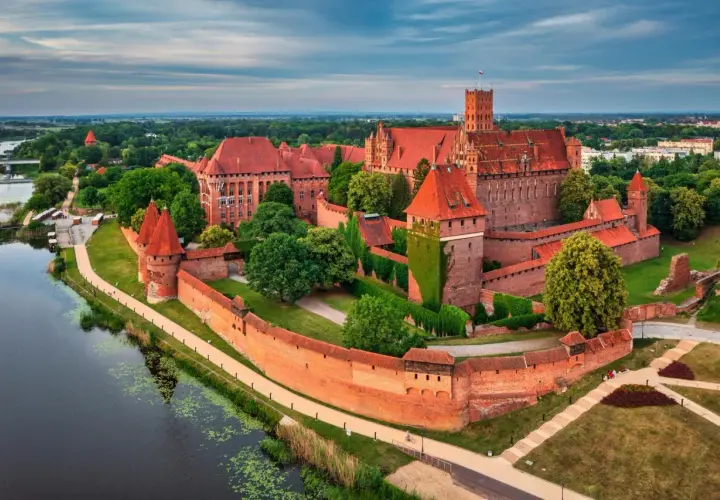 Malbork, największy zamek w Polsce, majestatycznie wznosi się nad rzeką Nogat. Potężne ceglane mury i liczne wieże świadczą o jego bogatej historii.