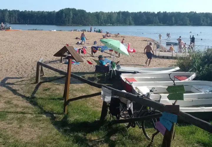 Słoneczny dzień nad zalewem zielona. Ludzie odpoczywają na plaży, kąpią się w wodzie, a obok cumują łódki.