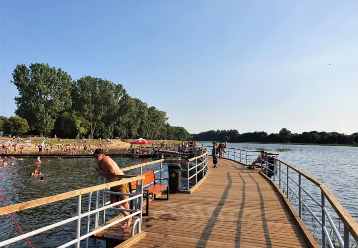 Ludzie odpoczywają i kąpią się nad zalewem Borki. Drewniane molo zaprasza do spacerów i podziwiania widoków.