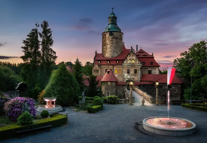 Zamek Czocha o zmierzchu, z fontannami i kwitnącymi rododendronami. Bilety do zamku można kupić online lub na miejscu.