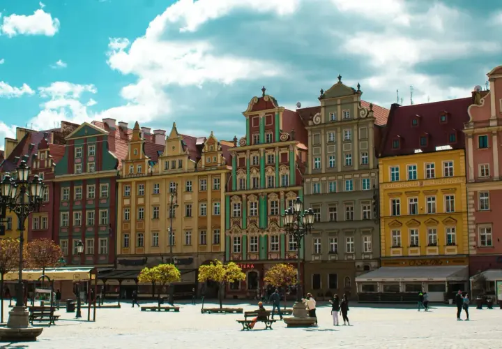 Kolorowe kamienice na starym rynku we Wrocławiu, z błękitnym niebem i białymi chmurami w tle.