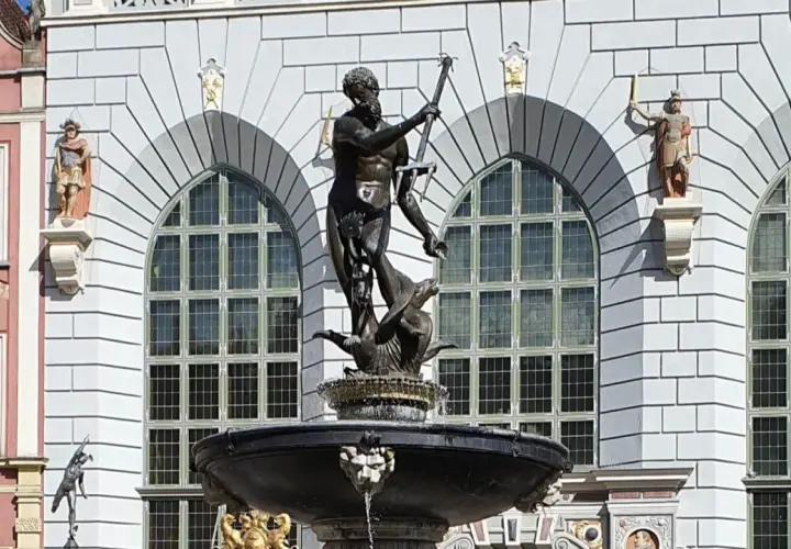 Fontanna Neptuna znajduje się w Gdańsku, przed fasadą budynku z arkadowymi oknami. Rzeźba przedstawia boga mórz na tle kamiennej architektury.