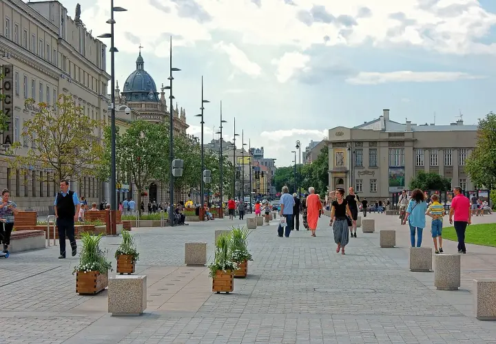Ludzie spacerują po pięknym, wybrukowanym placu Litewskim, otoczonym zabytkowymi budynkami i zielenią.