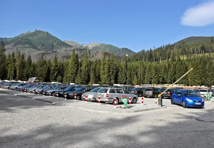 Parking pod Morskim Okiem, pełen samochodów, z górami i lasem w tle.