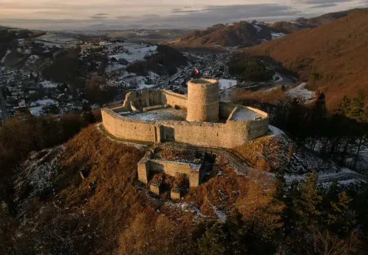 Zamek w Rytrze, kamienne ruiny na wzgórzu, z widokiem na dolinę i rzekę. Flaga Polski powiewa na wieży.