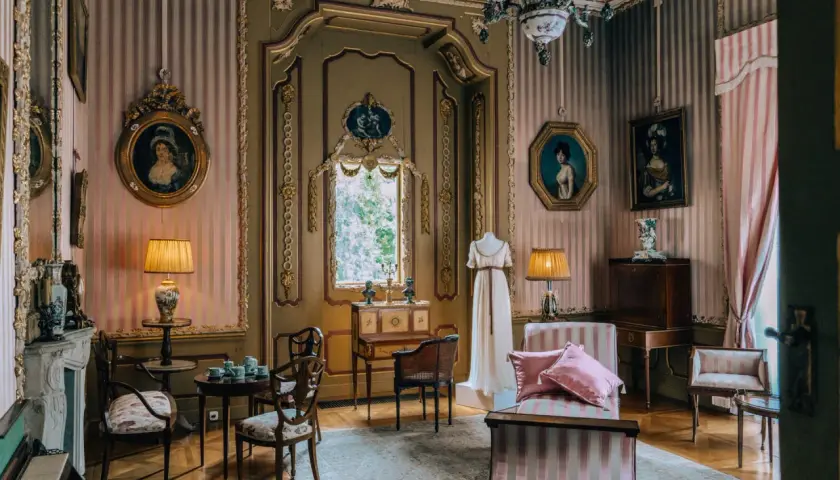 Eleganckie wnętrze pałacu w Nieborowie z portretami dam, manekinem w sukni i zabytkowymi meblami.