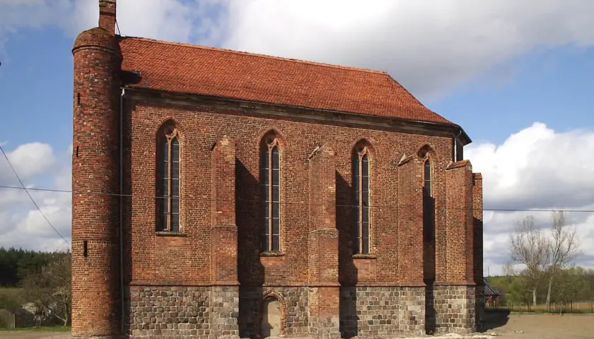 Gotycka budowla z cegły, przypominająca dawną warownię templariuszy, z charakterystyczną okrągłą wieżą i strzelistymi oknami.