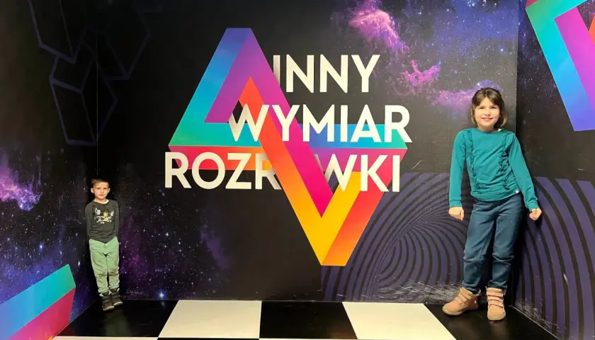 Dzieci w "Innym Wymiarze Rozrywki" w Warszawie. Kolorowa ściana z motywem kosmosu i geometrycznymi kształtami.