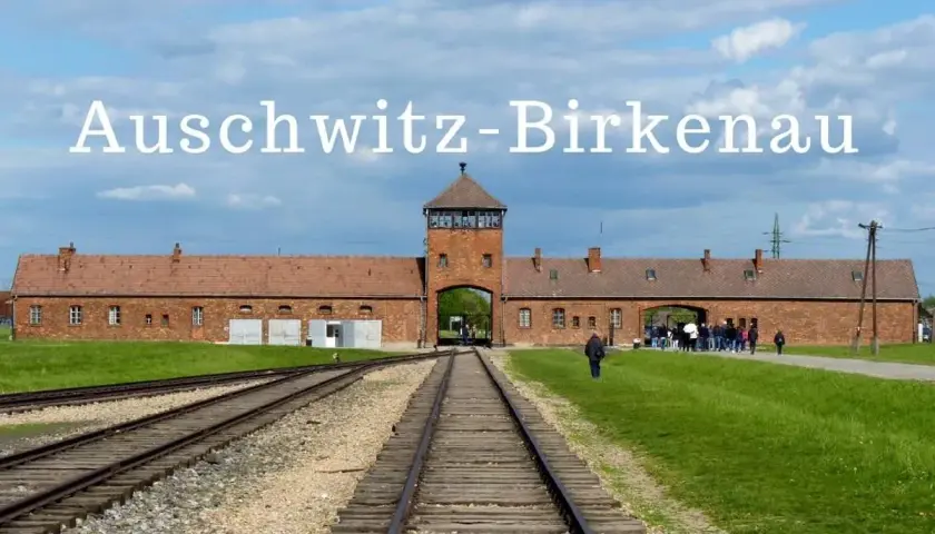 Brama obozu Auschwitz-Birkenau, gdzie jest to miejsce pamięci. Tłum zwiedzających podąża torami kolejowymi.