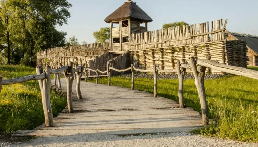 Drewniana kładka prowadzi do grodziska z wieżą obronną. To fragment szlaku piastowskiego, gdzie historia ożywa.