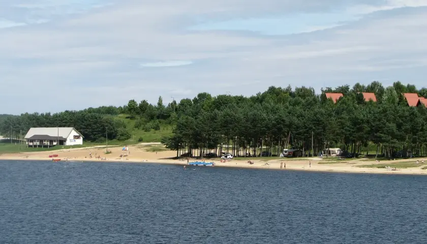 Słoneczny dzień nad zalewem Chańcza. Plaża z ludźmi, domki letniskowe i las.