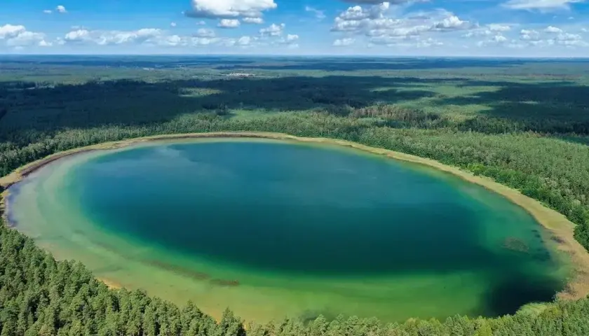Widok z lotu ptaka na owalne jezioro o turkusowej wodzie, otoczone gęstym lasem. To najczystsze jezioro w Polsce, zachwyca przejrzystością.