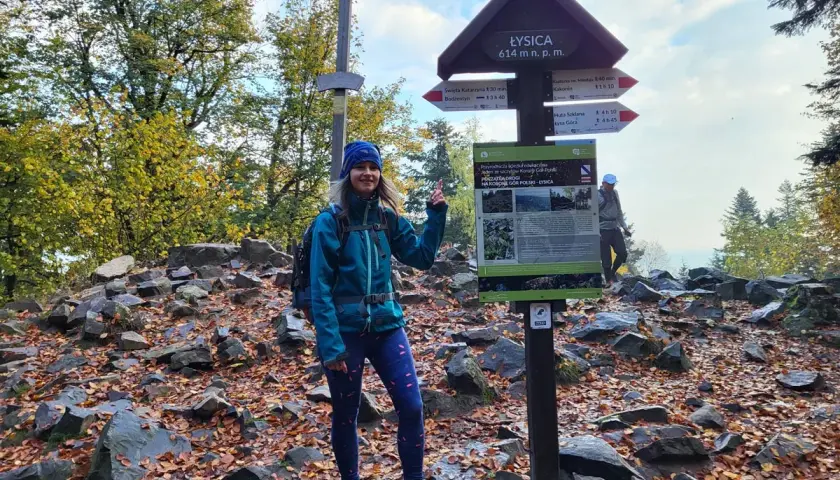 Kobieta na szczycie Łysica, 614 m n.p.m., wśród kamieni i jesiennych liści. Widoczny drogowskaz i krzyż.