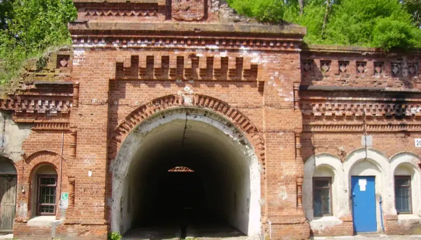 Wejście do tunelu w twierdzy Osowiec. Czerwona cegła, łukowate przejście, zieleń na dachu.