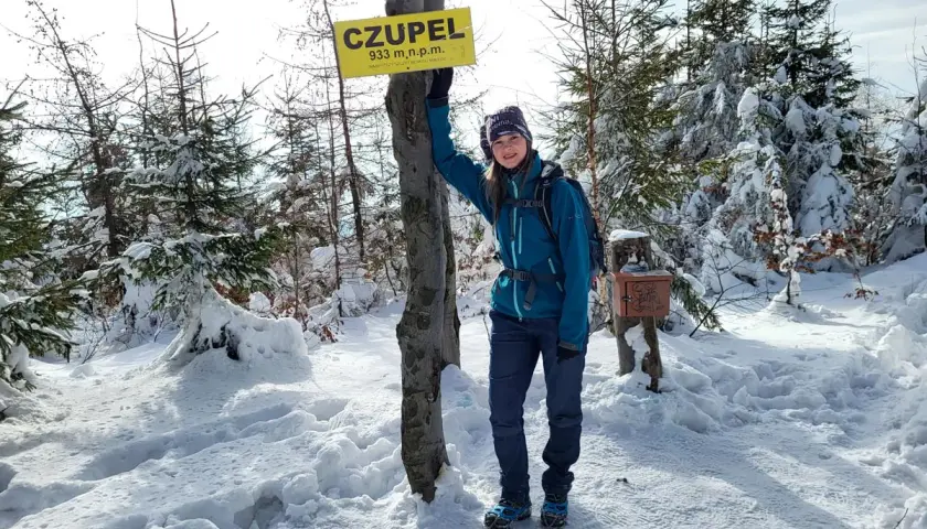 Dziewczyna stoi przy znaku "CZUPEL" w zimowym lesie.
