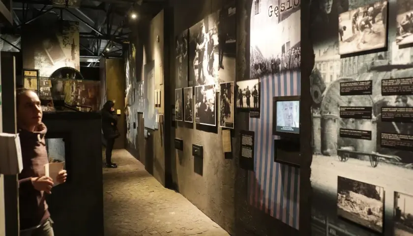 Wystawa w Muzeum Powstania Warszawskiego. Zwiedzający wpatrują się w historyczne fotografie i eksponaty, które budzą refleksje.