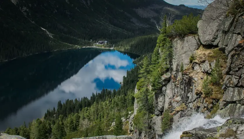 Widok na Morskie Oko z góry, z wodospadem po prawej. Trasa turystyczna prowadzi wzdłuż jeziora otoczonego lasem i górami.