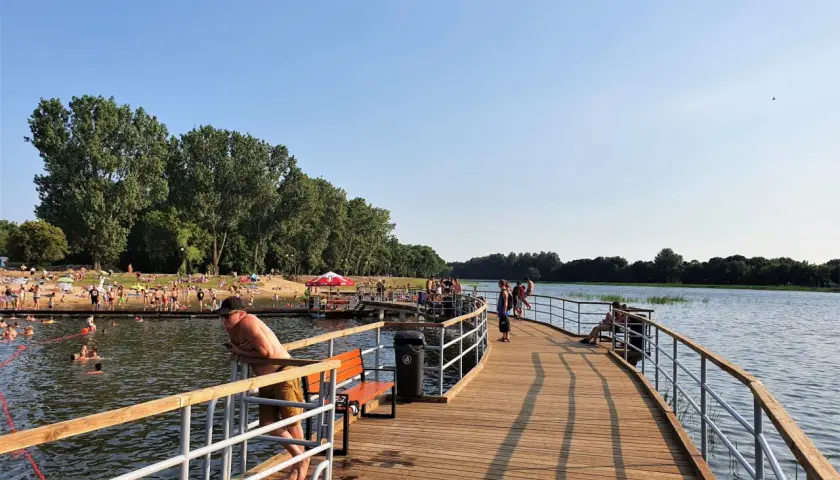 Ludzie odpoczywają i kąpią się nad zalewem Borki. Drewniane molo zaprasza do spacerów i podziwiania widoków.