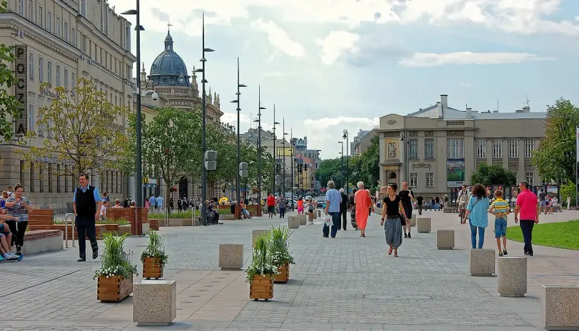 Ludzie spacerują po pięknym, wybrukowanym placu Litewskim, otoczonym zabytkowymi budynkami i zielenią.