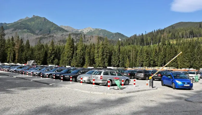 Parking pod Morskim Okiem, pełen samochodów, z górami i lasem w tle.