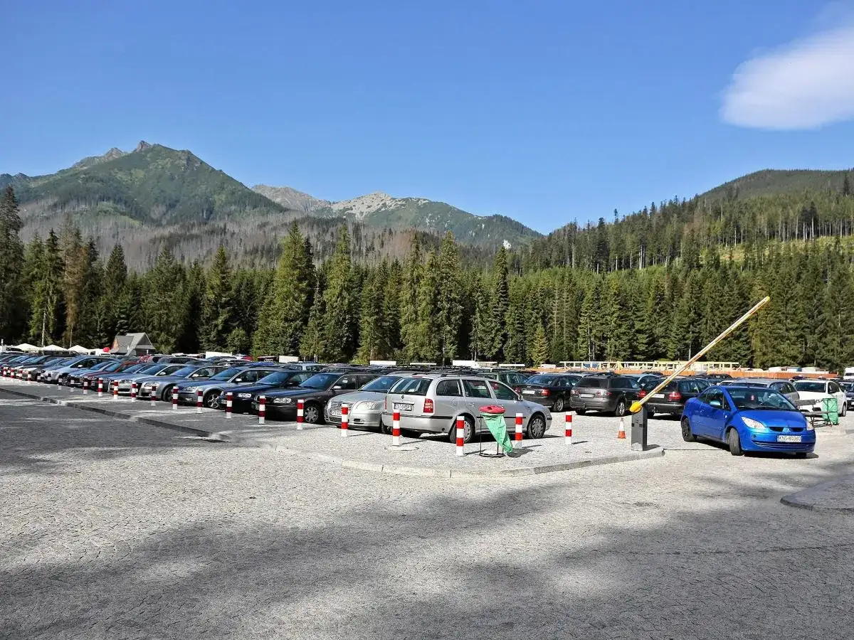 Parking pod Morskim Okiem, pełen samochodów, z górami i lasem w tle.