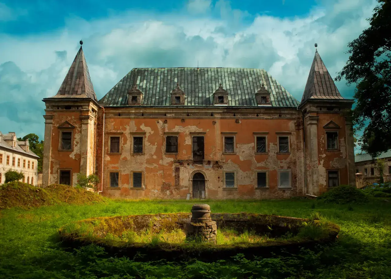 Zrujnowany pałac z wieżyczkami, porośnięty mchem i otoczony bujną zielenią. Kruszyna historii w zapomnianym miejscu.