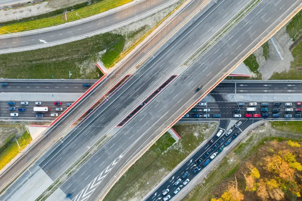Widok z lotu ptaka na wielopasmową drogę, która może być najdłuższą ulicą w Warszawie. Samochody poruszają się po betonowych pasach.