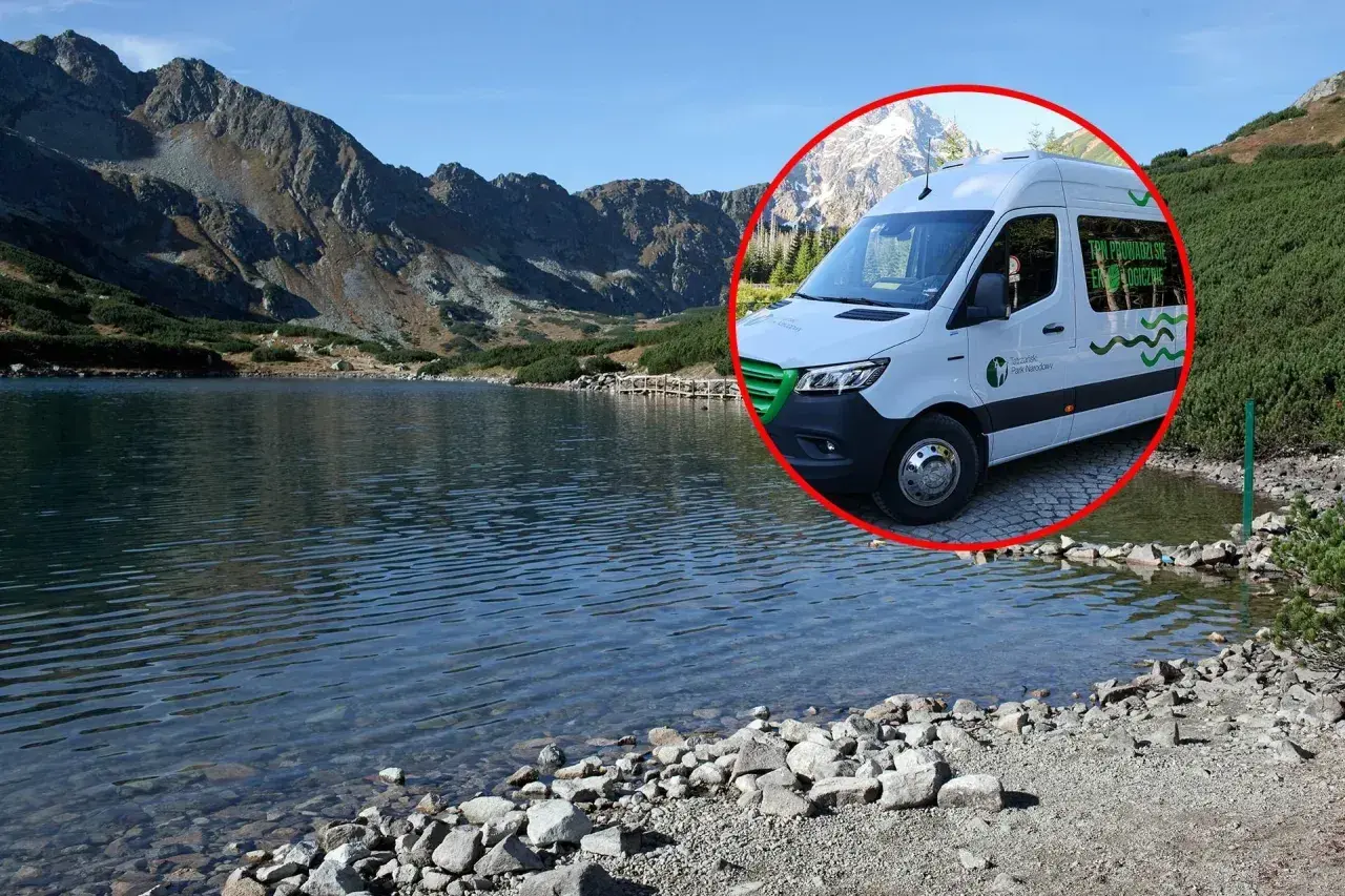 Biały bus do Morskiego Oka stoi przy tafli jeziora, w tle góry.