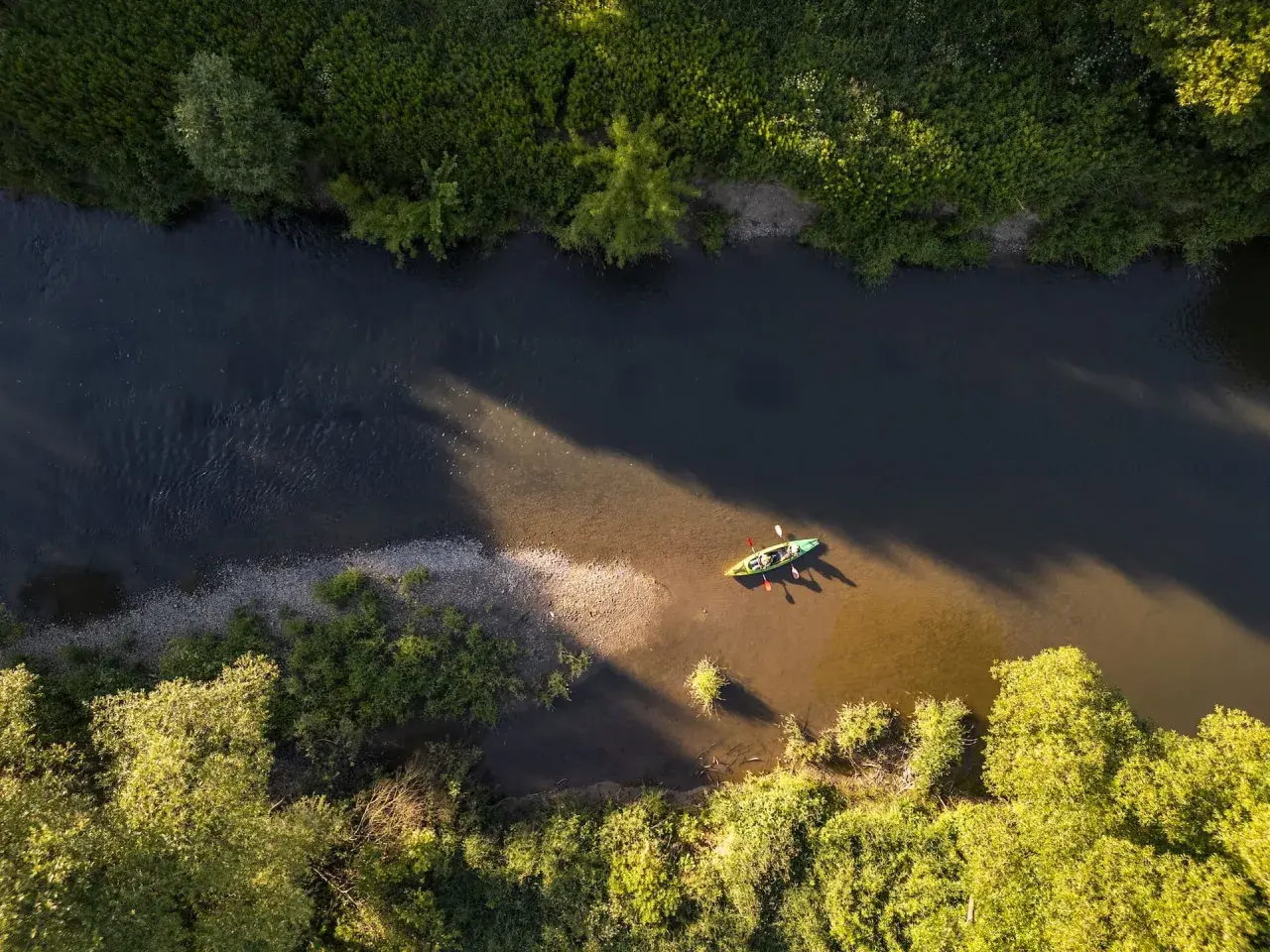 Dwie osoby płyną kajakiem po rzece w pobliżu Frysztaka, otoczeni bujną zielenią.